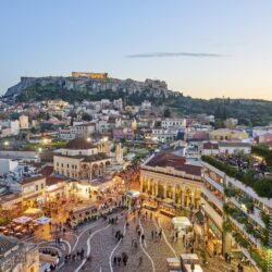 Athens, Greece - February 13, 2016: Aerial view of Athens at sunset with the Acropolis in the background. In foreground tourists and local people in Monastiraki Square. The clustered homes on the hill is known as Plaka.